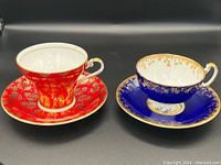 Red and cobalt blue Aynsley teacups with matching saucers showing gold leaf and gold gilt designs.