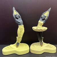 Front view of both ballet dancer figures side by side on dark background, showing full height and painted details.