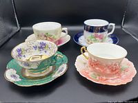 Four hand-painted porcelain teacups and saucers showing floral designs and gold gilt detailing with pink, green, blue and white colors