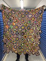 Full view of the large crochet blanket held by a person for scale, showcasing the colorful rainbow square pattern and scalloped edge.