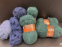 Photo showing 7 skeins of wool yarn in green and blue colors, with 4 green skeins labeled 'Iceland Lopi' and 3 blue skeins unlabeled.