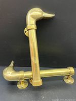 Two large vintage brass door handles with detailed duck head ends shown standing upright on a black surface.