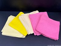 Photo showing groups of folded linen napkins in cream, yellow, and pink colors.