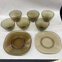 Front view of six smoke glass bowls and four square curved edge brown smoke glass plates showing the entire lot.