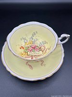 Top angled view of teacup inside saucer showing floral design with 'Mother' and pale yellow background with gold trim.
