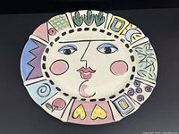 Front view of large ceramic platter showing abstract face center and colorful geometric border