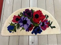 Top down view of the semi-circular latch hook rug laid flat showing colorful floral design on cream background.