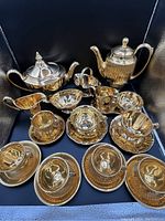 Tea and coffee set items displayed on a black background showing gold luster finish