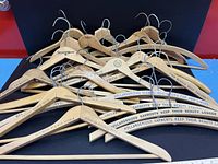 Lot of vintage wooden hangers on black surface, showing multiple hangers stacked together with metal hooks visible, advertising text visible on many hangers.
