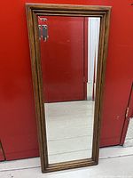 Full view of the rectangular vintage mirror leaning against a red wall, showing overall shape and frame design.