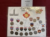 Coins from Canadian provinces displayed on a printed map with provincial shields and abbreviations, including a central display with a special coin and maple leaf graphic.