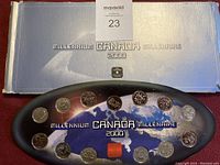 Oval black display holding 12 Canadian Millennium 2000 coins in original box with silver and blue gradient cover and text.