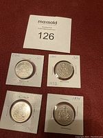 Four Canadian fifty cent coins in held protective cardboard coin holders with dates 1972, 1974, 1983 and one partially visible date.