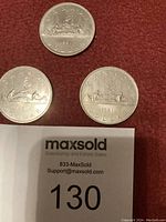 Three 1981 Canadian one dollar coins arranged on a red fabric background with MaxSold lot number tag visible.