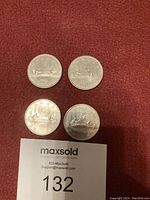 Four Canadian one dollar coins with Voyageur design on red background, along with a MaxSold tag with number 132.