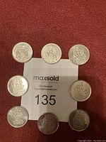 Photo of eight Canadian fifty cent coins arranged on red fabric, showing coat of arms side.