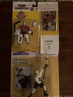 Photo showing two packaged 1995 Starting Lineup 4th Edition hockey figures: Martin Brodeur in red goalie gear and Paul Kariya in white black uniform holding a hockey stick. Both figures come with cards and original packaging in good visible condition.