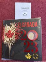 Black O Canada 2023 tri-fold folder with gold and red maple leaf fireworks design, official Canadian coin set from Royal Canadian Mint.