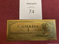 Front side of the gold plated Canadian one dollar bill replica showing text, signatures and Queen Elizabeth II profile.