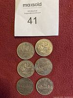 Photo of six Canadian one dollar coins from years 1968, 1970 (x2), 1982 (x2), and 1983 showing various commemorative designs including sailboat and floral emblems.