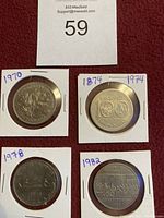 Four one dollar coins in protective holders dated 1874, 1970, 1974, 1978, and 1982, shown on red cloth background with auction number 59 tag.