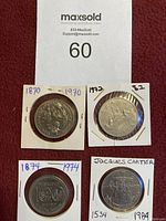 Four one dollar coins each in white cardboard holders with handwritten years, including '1870-1970', '1973-82', '1874-1974 Winnipeg 50th Anniversary', and 'Jacques Cartier 1534-1984'. Coins are metallic with varied engraving.