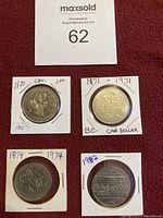 Four Canadian one dollar coins in white protective holders displayed on a red background with MaxSold lot number 62.