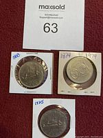 Four one dollar coins in protective holders with noted years 1874, 1968, 1974, and 1975, showing front and back designs with Canadian motifs including loons and ships.