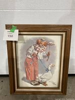 Framed picture showing a clown holding a red and white umbrella and a feather on a stick next to a white duck on a leash.