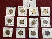 Lot of 12 USA state quarter dollar coins individually placed in white cardboard holders with state names handwritten on each holder.