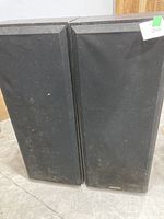 Photo of two tall floor-standing speakers placed side by side, with black fabric grille covers.