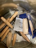 Top-down view inside a round Christmas-themed tin showing multiple wood carving tools with wooden handles and blue plastic blade covers.