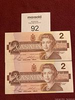 Front view of two Canadian 2 dollar bills, showing Queen Elizabeth II portrait and denomination.