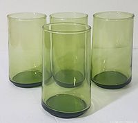 Four avocado green vintage blown glass beverage glasses of cylindrical shape, displayed together on white surface.