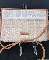 Front view of the handbag showing woven beige fabric and sakroots leather brand patch.