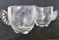Two pieces of clear etched crystal Paden City Glass: a creamer and an open sugar bowl with floral patterns and decorative side handles, photographed against a black background.