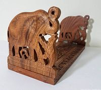 Front angle view showing one carved elephant end and the wooden slat base of expandable book rack.