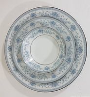 Three pieces stacked to show scale and pattern detail: dinner plate, salad plate, fruit/dessert bowl with blue floral pattern and platinum trim.