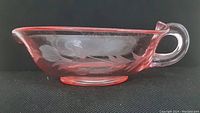 Side view of the pink Depression glass bowl showing the etched leaf pattern and single clear loop handle.