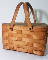 Front view of vintage woven wood picnic basket with two wooden handles and hinged lid closed, showing basket texture and construction.