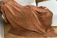 View of the full shawl spread out displaying its large size and intricate paisley pattern in reddish-orange and earth tones