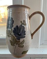 Full view of the tall ceramic pitcher/jug with hand painted blue flowers and handle.