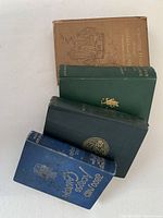 Top view of five antique books stacked vertically against a white background showing color and cover details