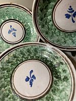 Close-up view of the top three plates showing hand-painted blue floral design in center, green sponge-effect border, and ceramic wear.