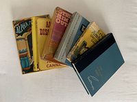 Seven vintage hardcover books on white surface, visible titles and worn dust jackets, some taped.