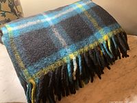 Vintage wool blanket showing Campbell clan tartan pattern with black, blue, yellow, and gray colors and fringed edges.
