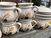 Close-up of six cream-colored pottery cups stacked, showing floral decorative motif in yellow, brown, and blue.