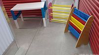 Overall view of the children's table, shoe rack, and book holder in storage unit.