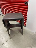 Full view of gray steel rolling cart showing one drop-leaf side extended and the other folded down on wheels.