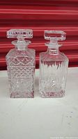 Front view of two squared lead crystal whiskey decanters with detailed cut designs and large square stoppers.